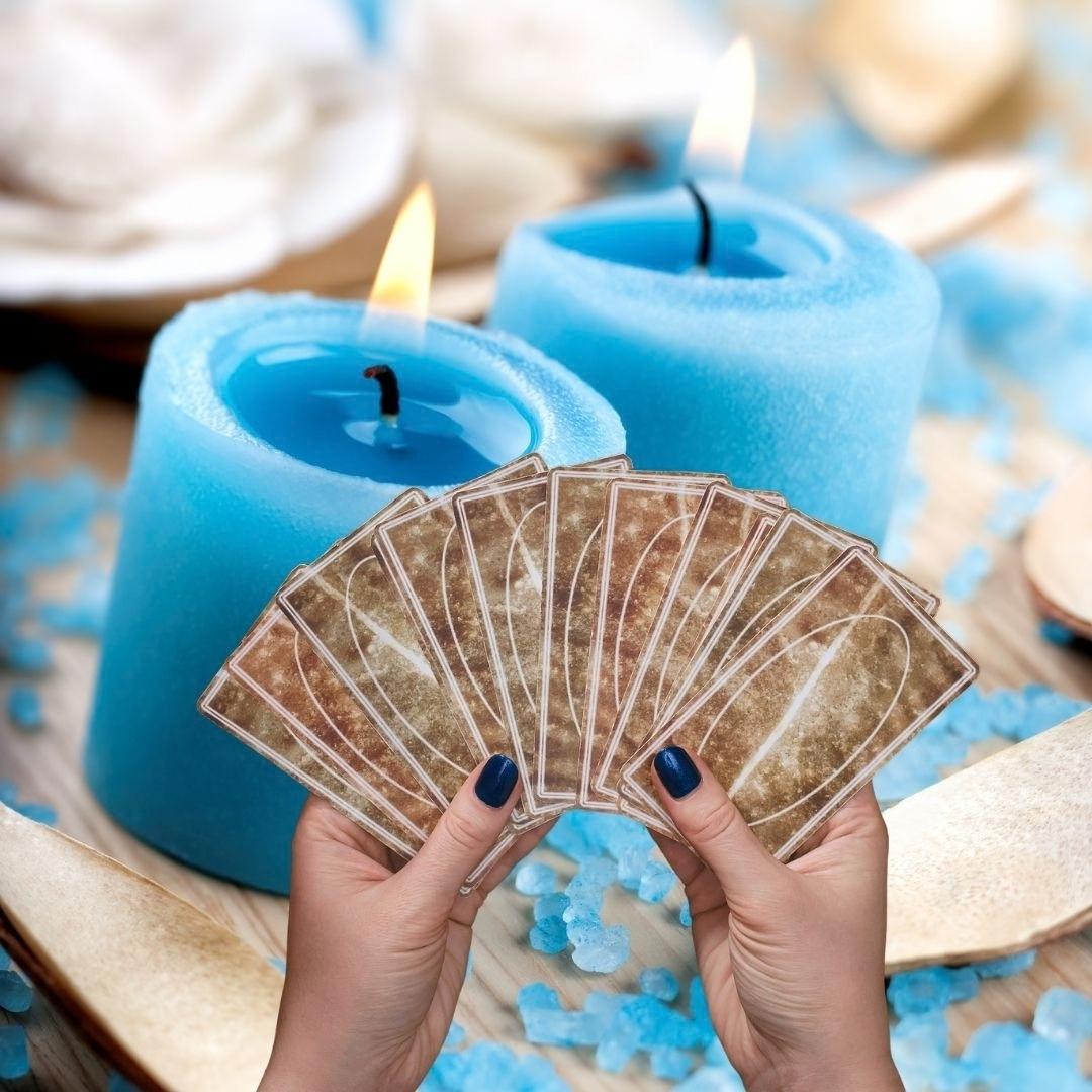 Fotografía publicitaria de lectura de cartas del tarot con velas rituales azules e iluminación cálida.